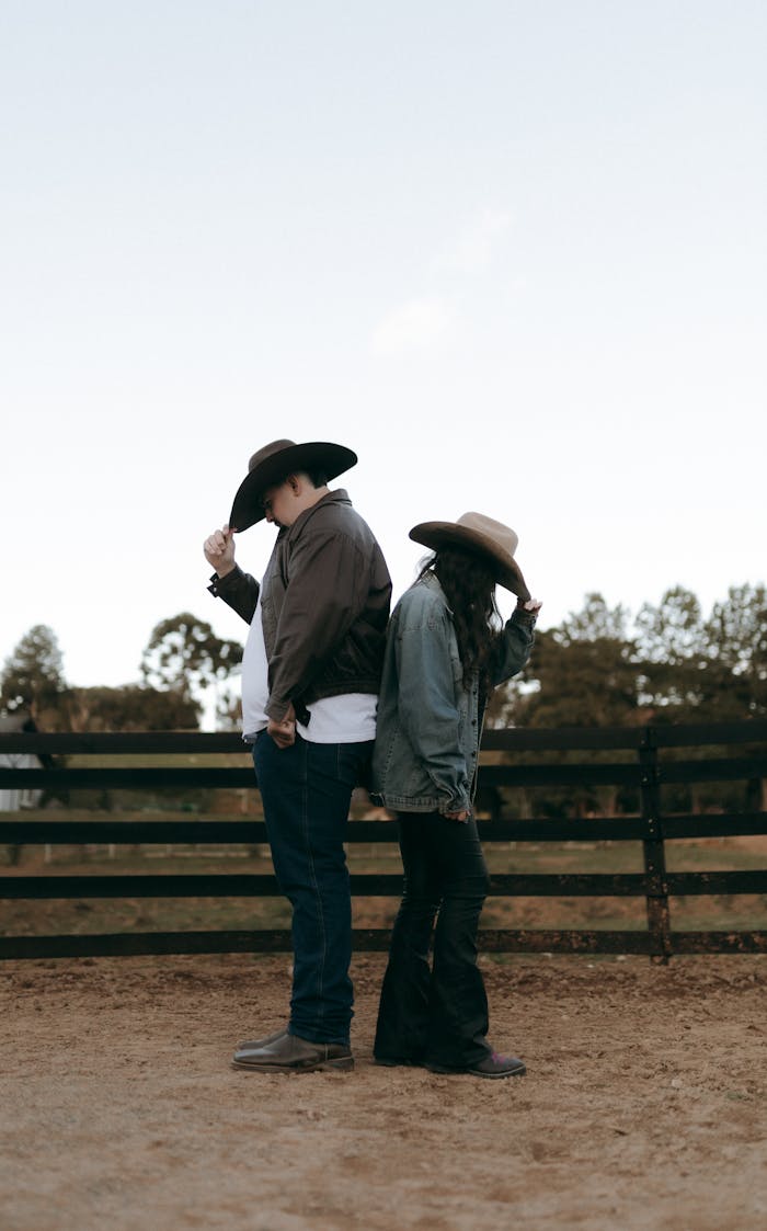 Two cowboys standing back-to-back in a rural setting, evoking a western theme.