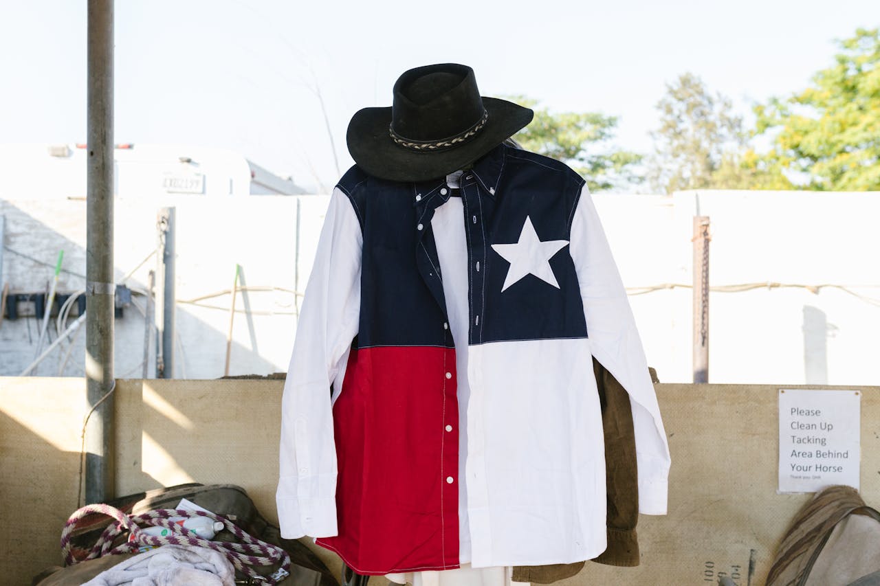 A Texas flag shirt and cowboy hat hanging outside. Represents Western fashion and lifestyle.